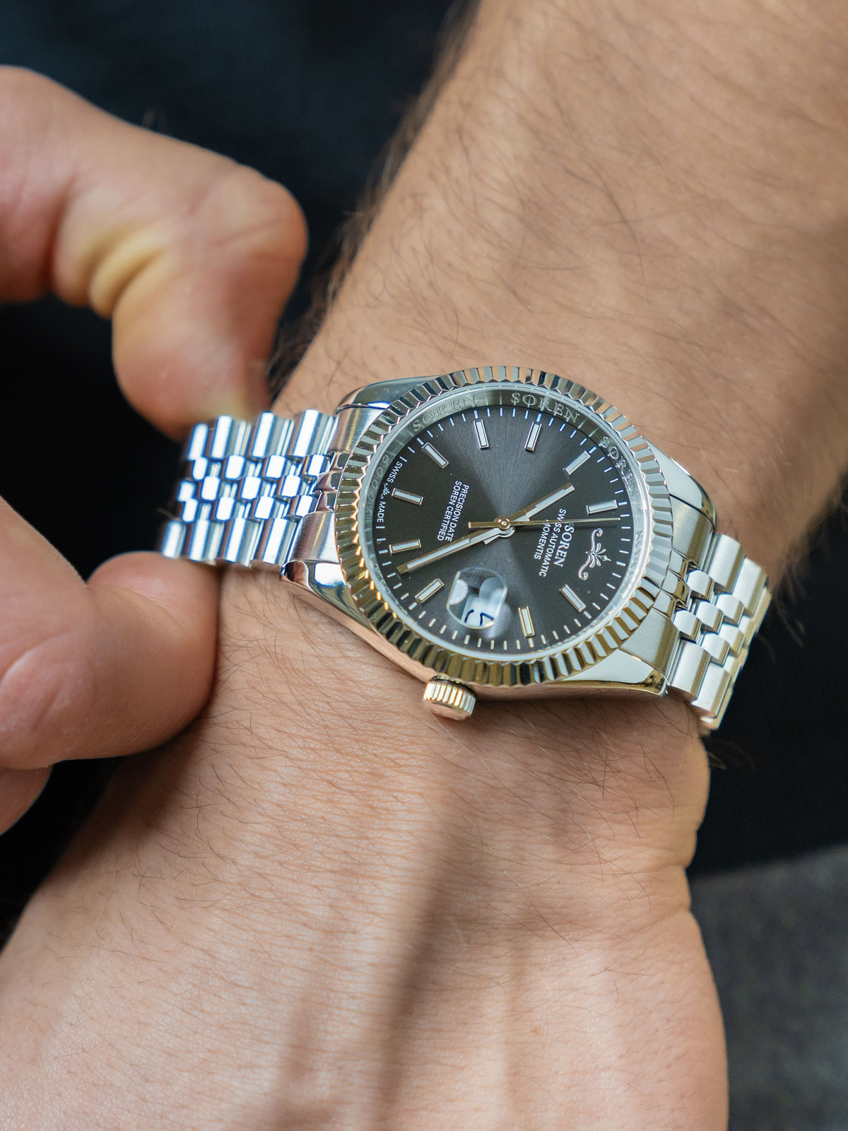 Man adjusting the 5-link steel bracelet of the SOREN Momentis Swiss automatic watch with black dial