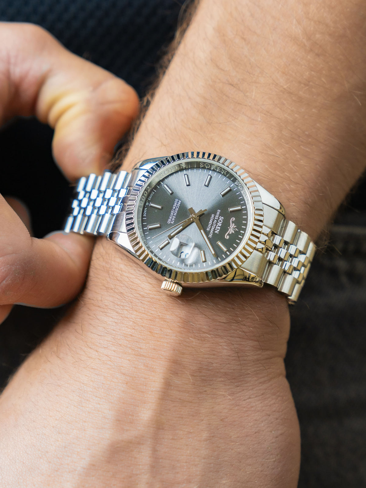 Man adjusting the 5-link steel bracelet of the SOREN Momentis Swiss automatic watch with grey dial
