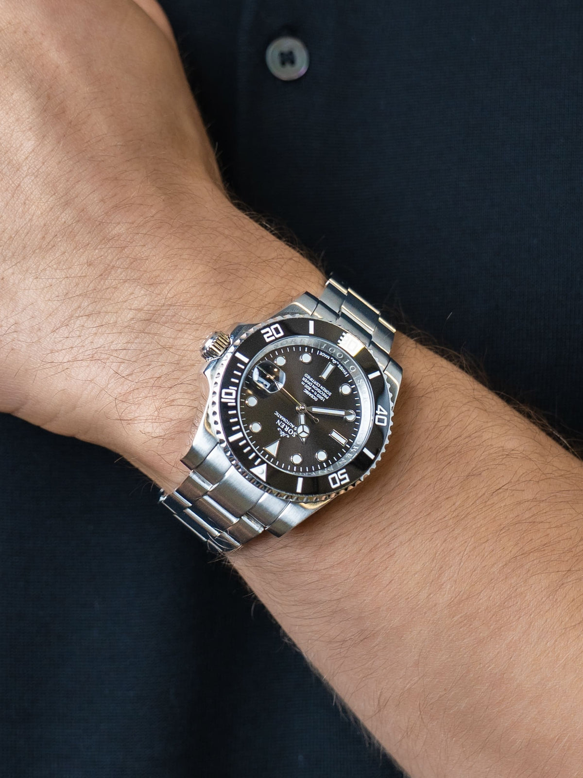 Man wearing the SOREN Oceanic Swiss automatic dive watch, black dial on a 3-link steel bracelet, with hand resting on his chest