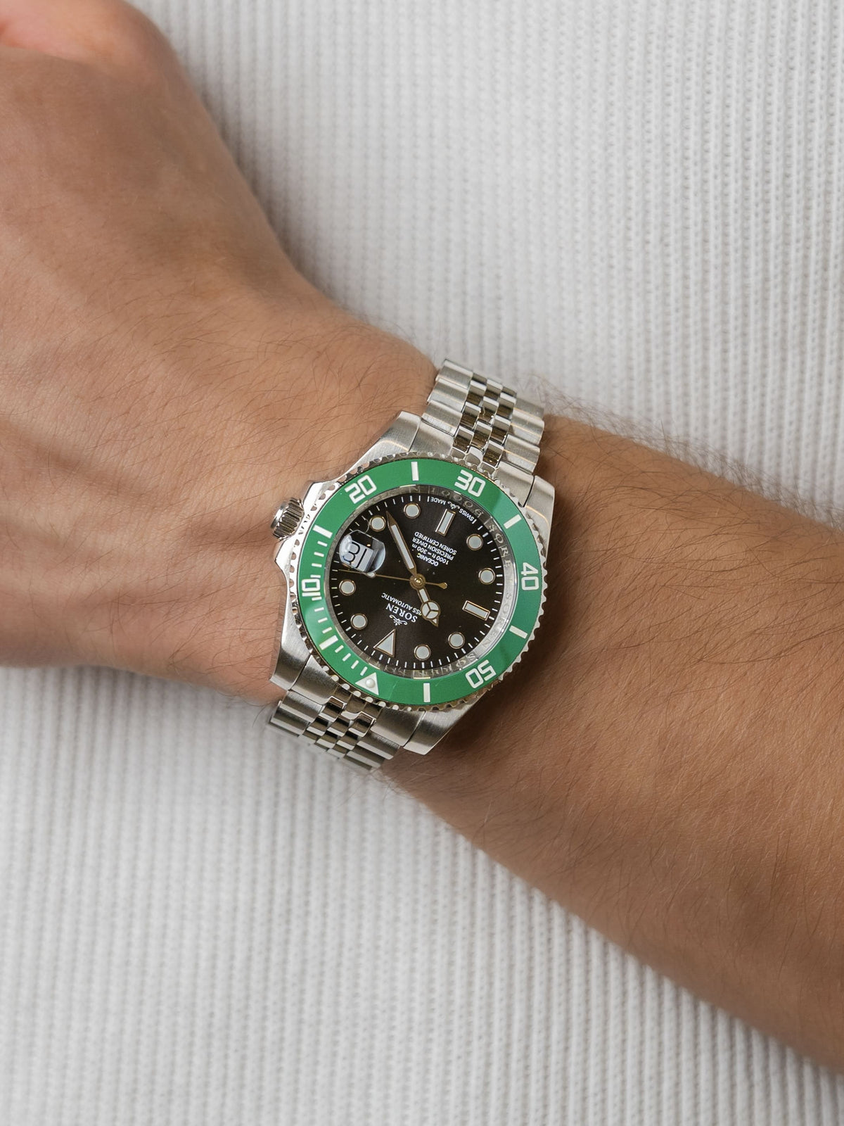Man wearing the SOREN Oceanic Swiss automatic dive watch, green bezel and black dial on a 5-link steel bracelet, with hand resting on his chest