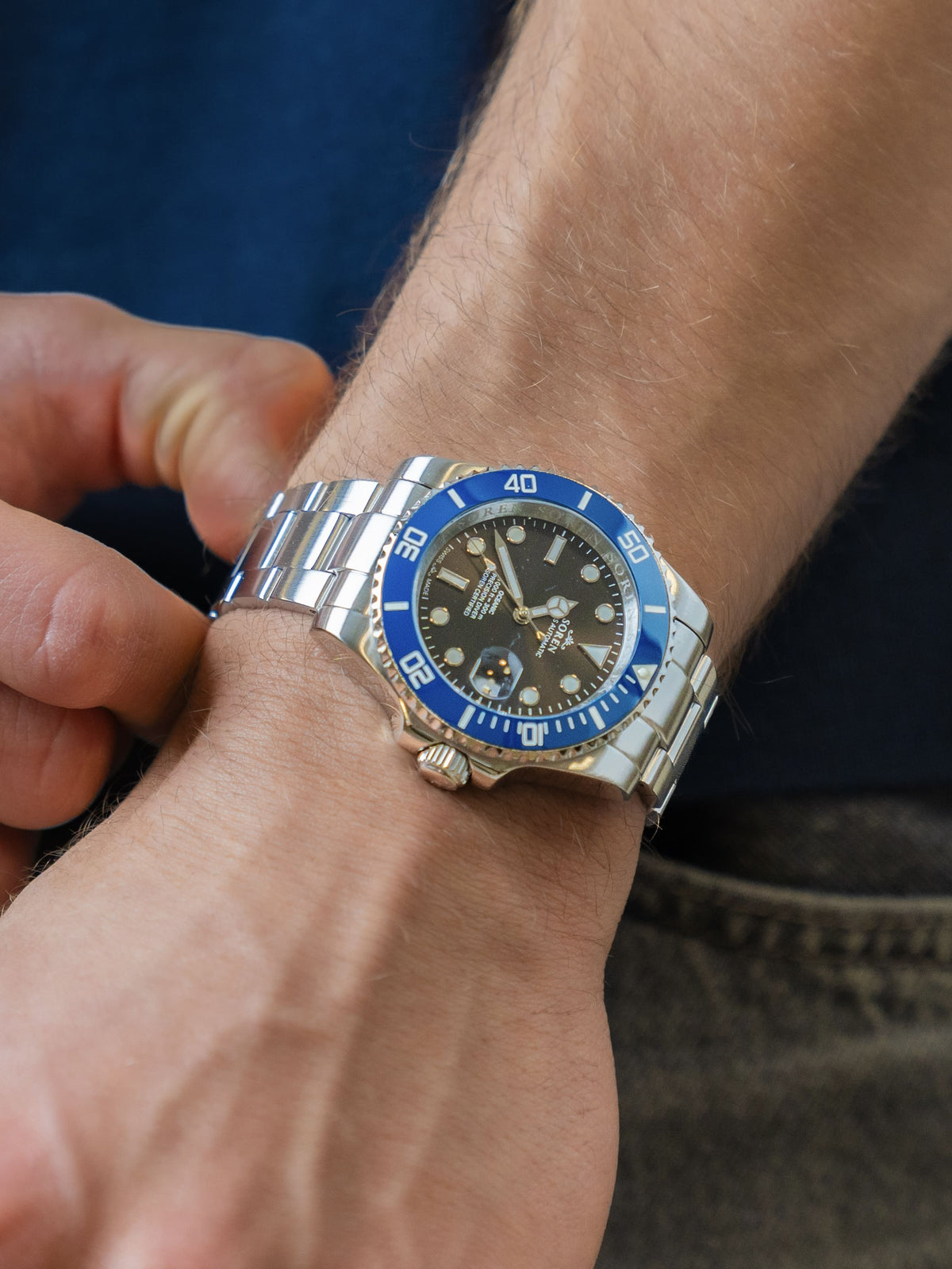 Man adjusting the 3-link steel bracelet of the SOREN Oceanic Swiss automatic dive watch with a blue bezel

