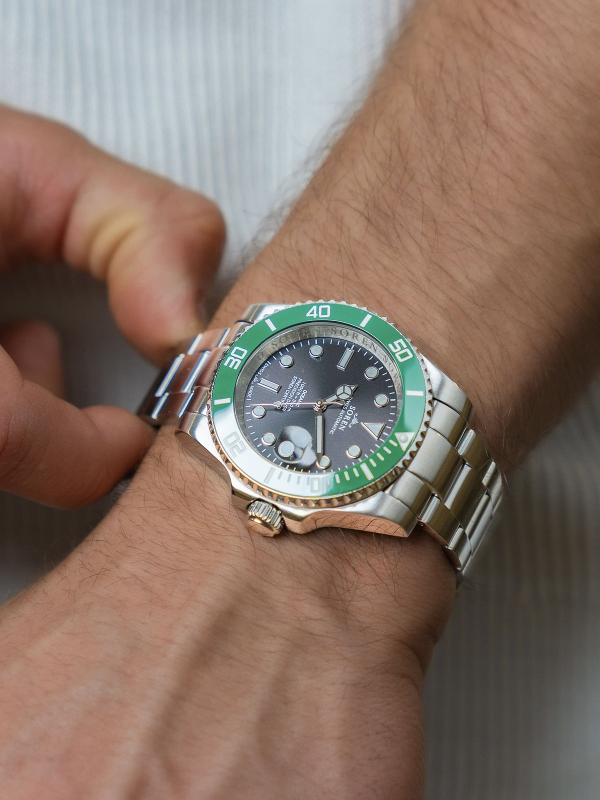 Man adjusting the 3-link steel bracelet of the SOREN Oceanic Swiss automatic dive watch with a green bezel

