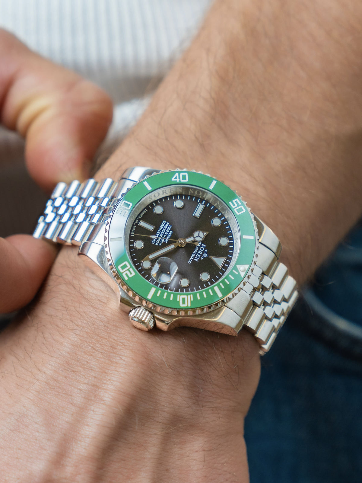 Man adjusting the 5-link steel bracelet of the SOREN Oceanic Swiss automatic dive watch with a green bezel and black dial
