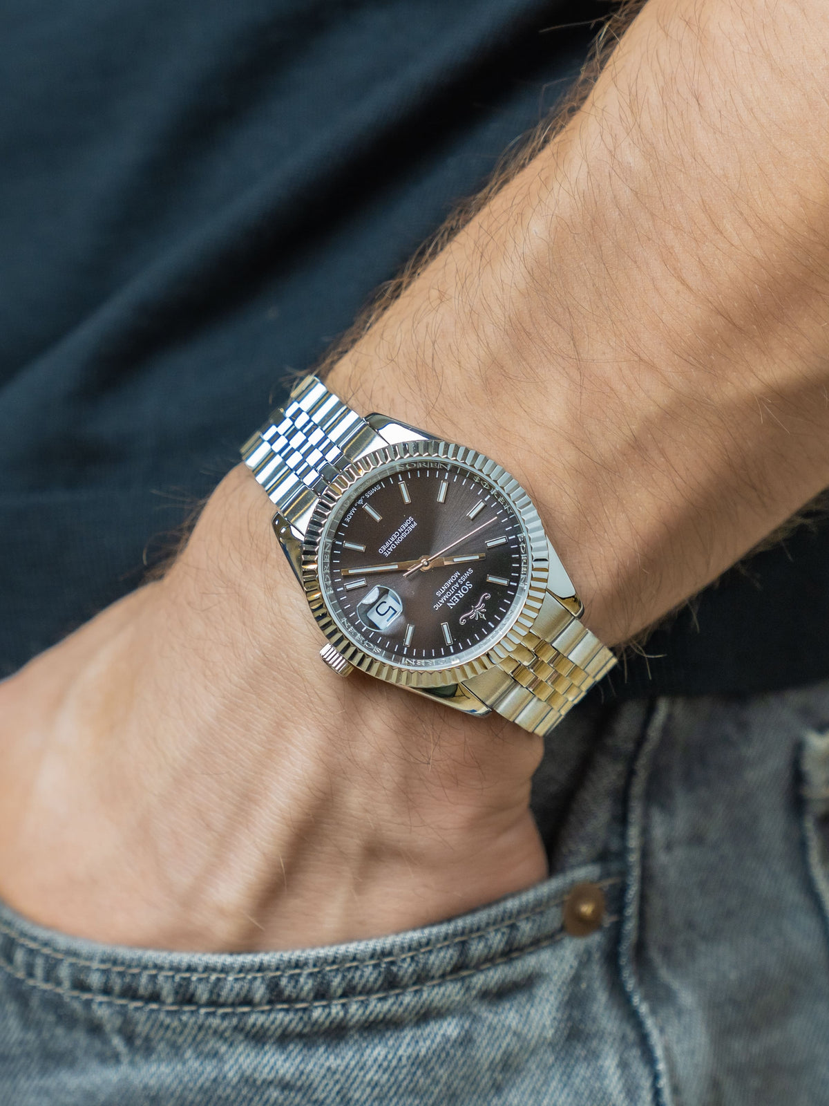SOREN Momentis Swiss automatic watch with black dial on a 5-link steel bracelet, worn on the wrist with hand in pocket
