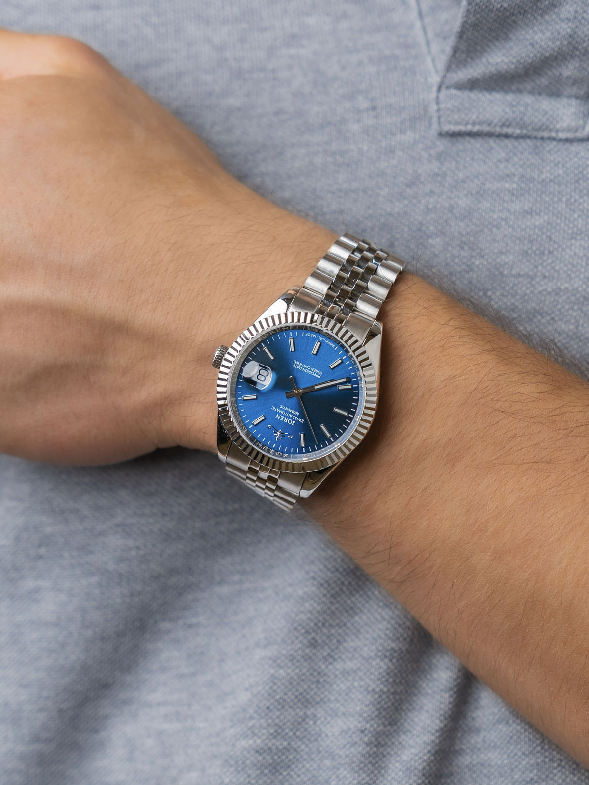 Man wearing the SOREN Momentis Swiss automatic watch, blue dial on a 5-link steel bracelet, with hand resting on his chest