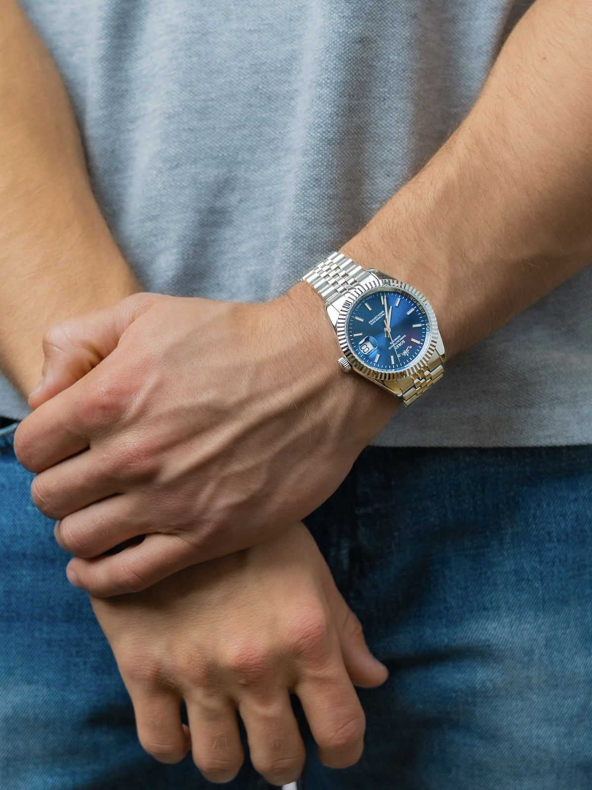 SOREN Momentis Swiss automatic watch with blue dial on a 5-link steel bracelet, shown with hands clasped together
