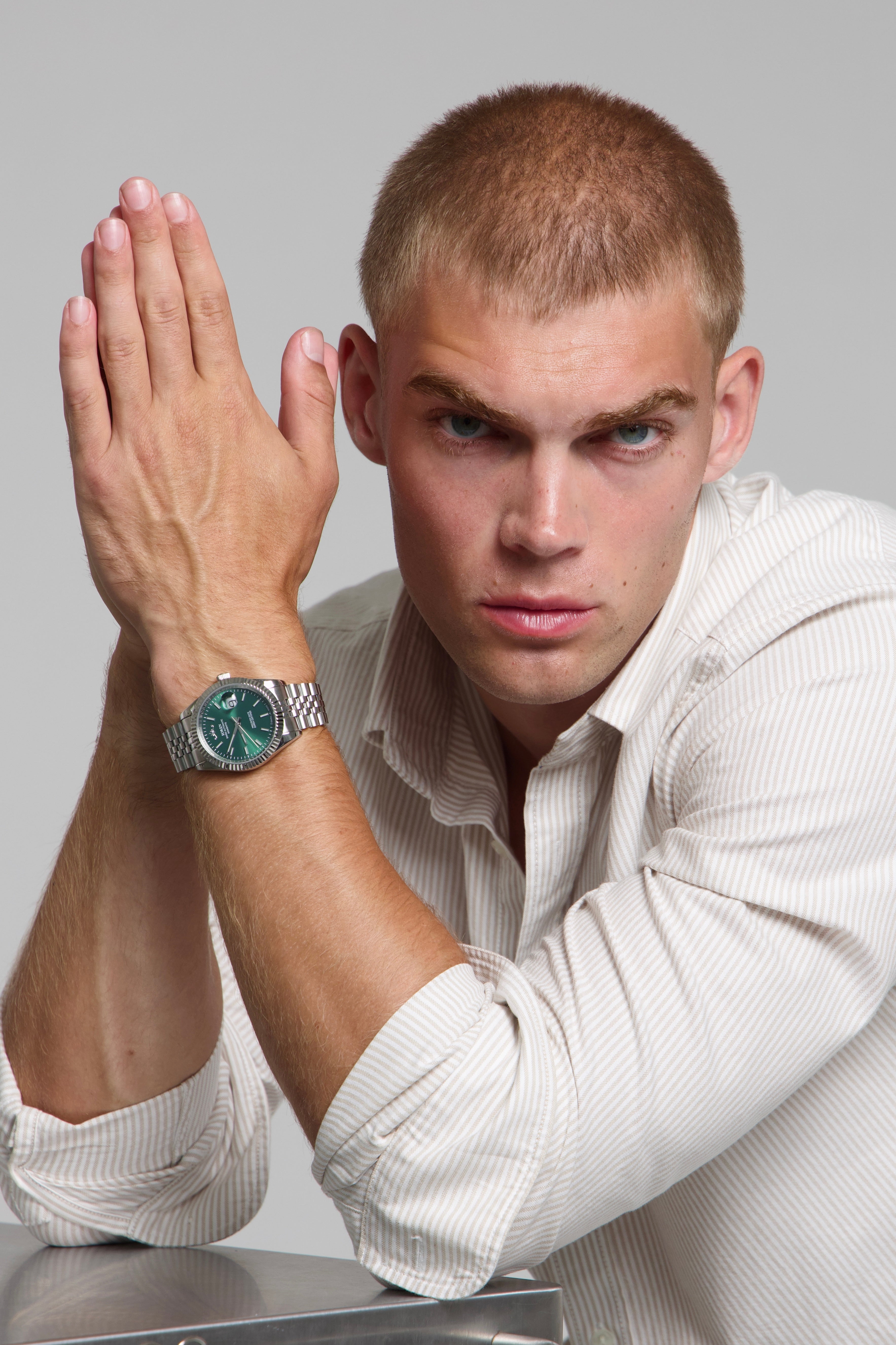 Man wearing a SOREN Momentis green watch on a jubilee bracelet, seated with his arms on a table
