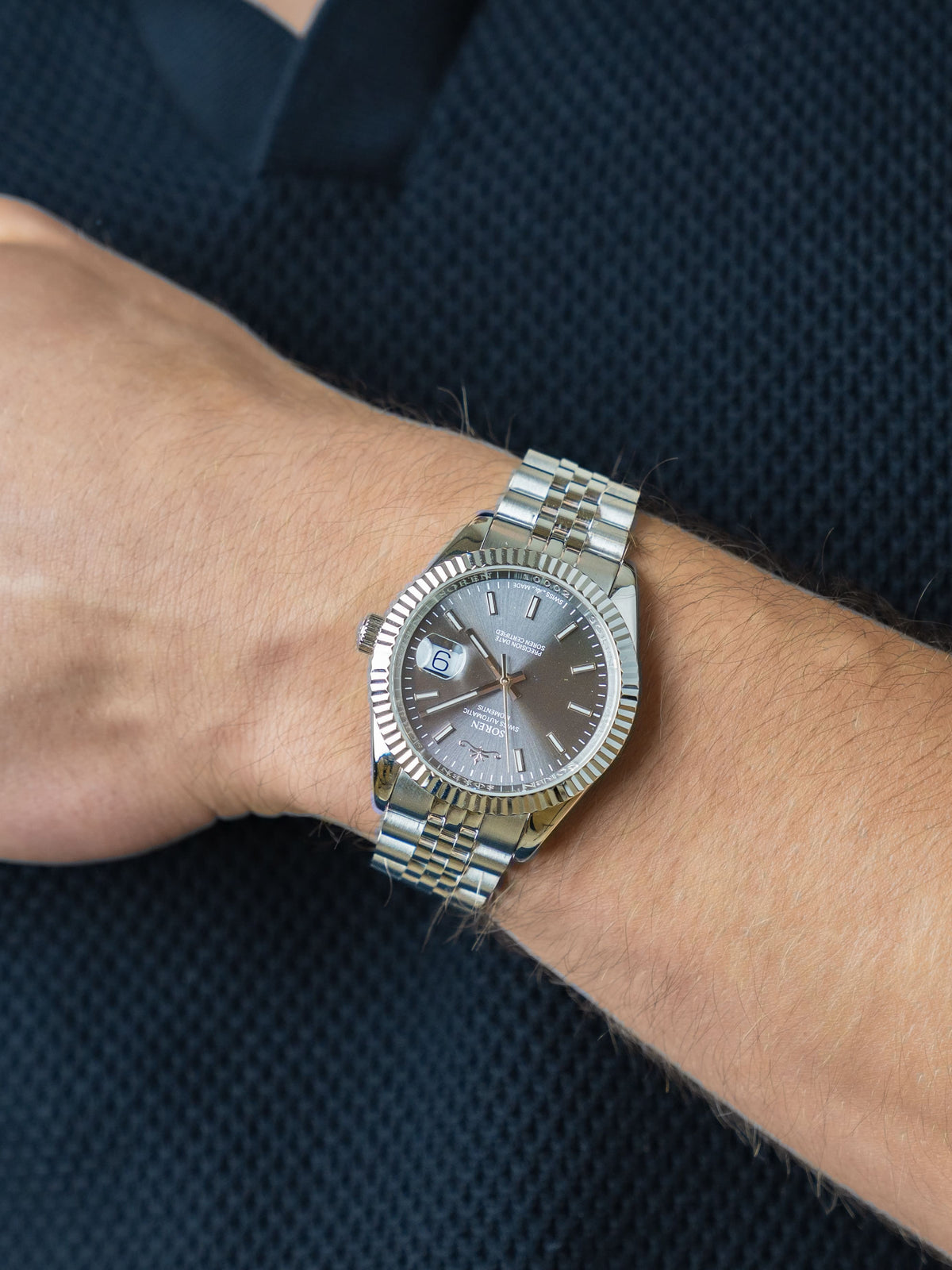 Man wearing the SOREN Momentis Swiss automatic watch, grey dial on a 5-link steel bracelet, with hand resting on his chest