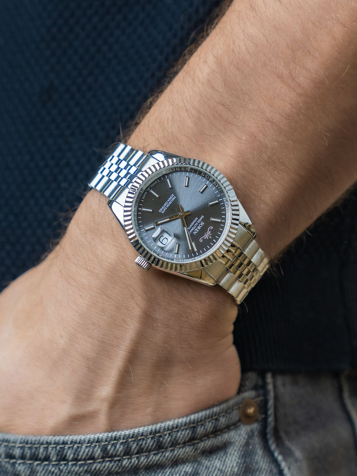 SOREN Momentis Swiss automatic watch with grey dial on a 5-link steel bracelet, worn on the wrist with hand in pocket
