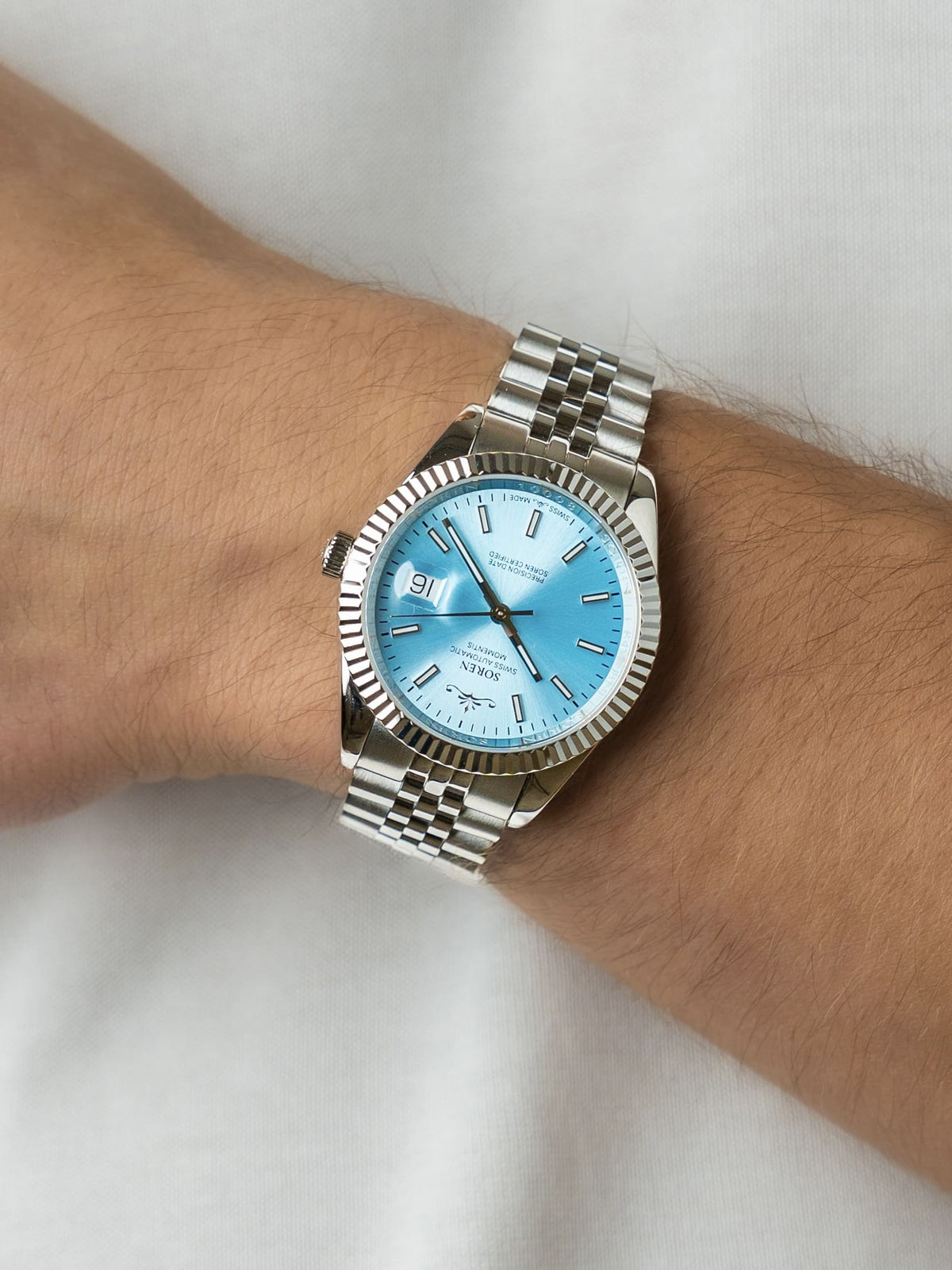Man wearing the SOREN Momentis Swiss automatic watch, ice blue dial on a 5-link steel bracelet, with hand resting on his chest