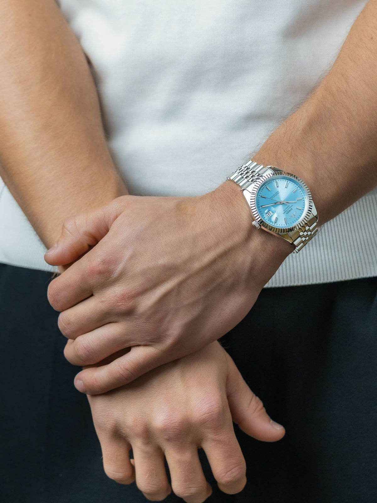 SOREN Momentis Swiss automatic watch with ice blue dial on a 5-link steel bracelet, shown with hands clasped together

