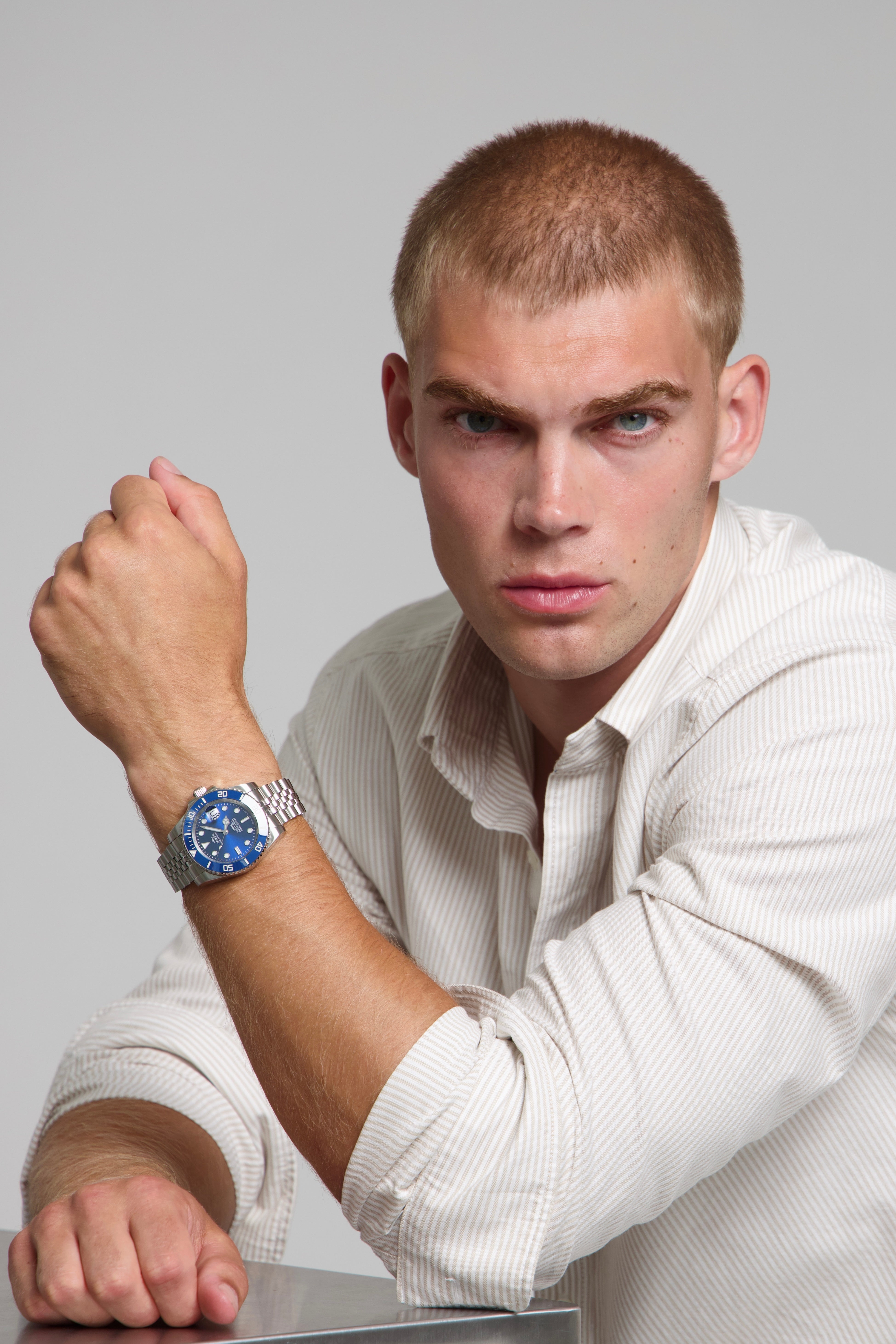 Man wearing a SOREN oceanic all blue watch on a jubilee bracelet, seated with his arm on a table
