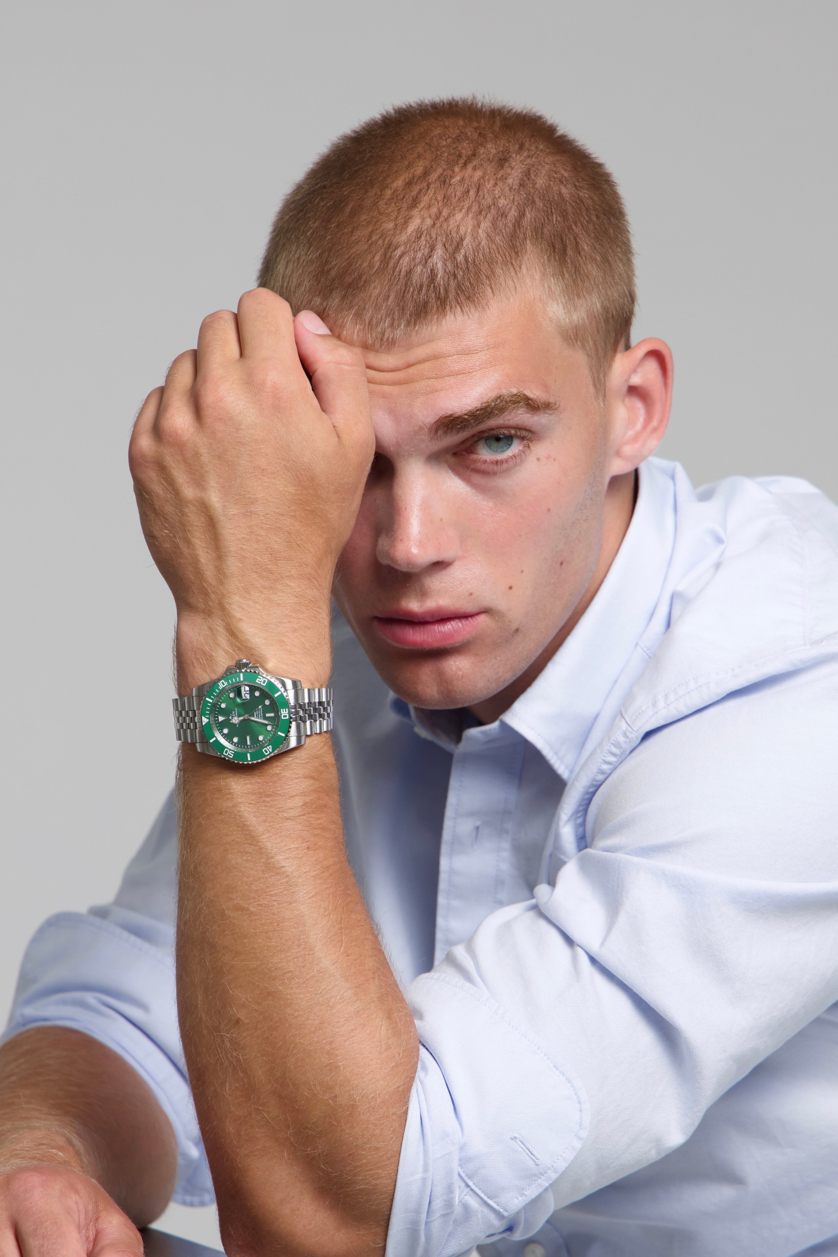 Man wearing a SOREN oceanic all green watch on a jubilee bracelet, seated with his arm on a table
