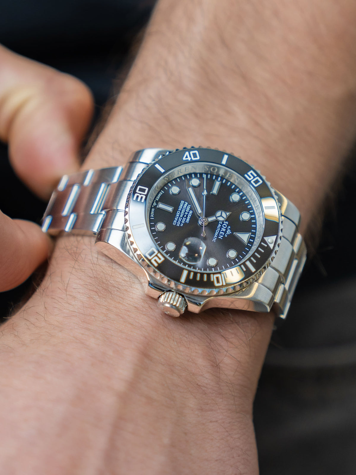 Man adjusting the 3-link steel bracelet of the SOREN Oceanic Swiss automatic dive watch with black dial
