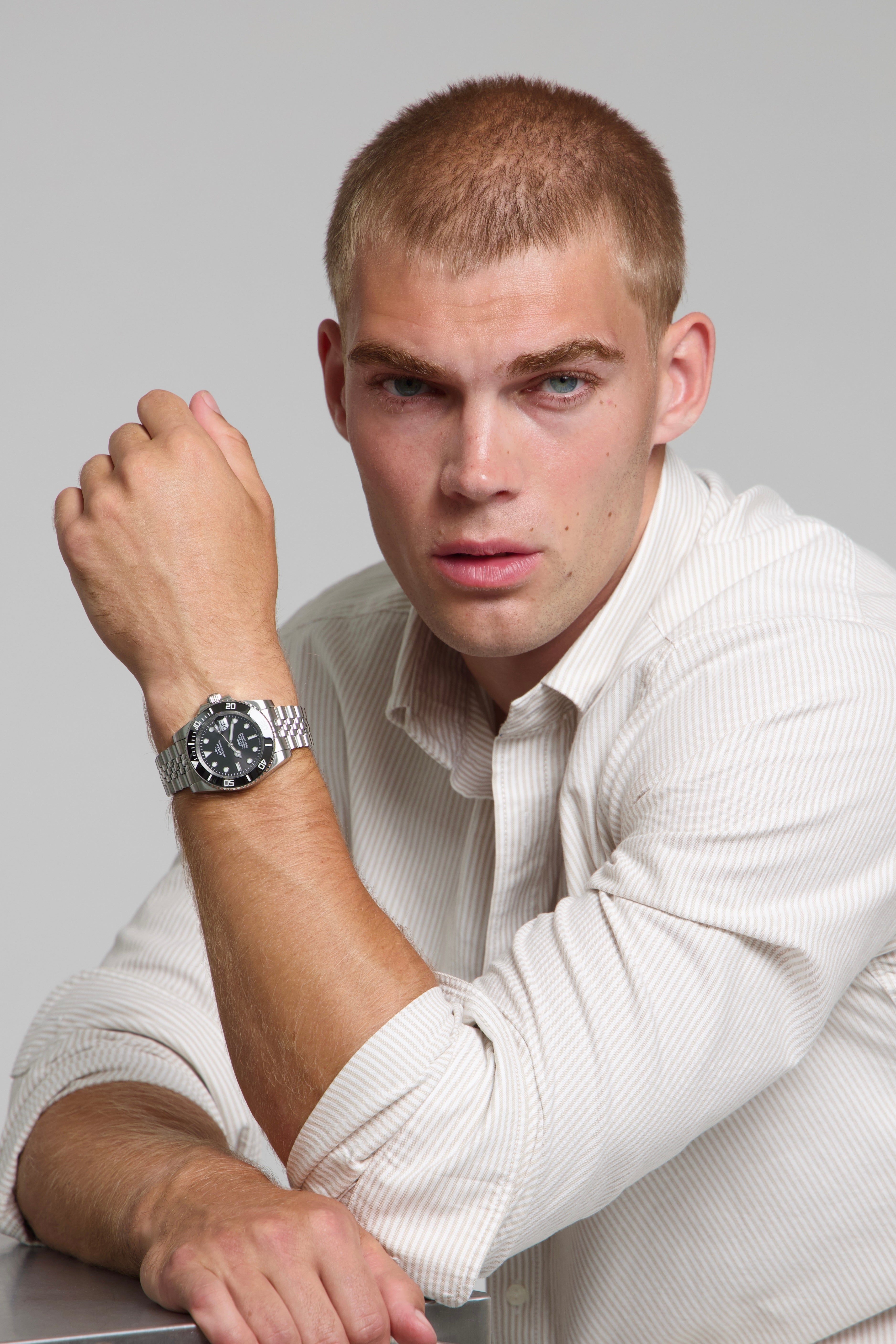 Man wearing a SOREN oceanic black watch on a jubilee bracelet, seated with his arm on a table
