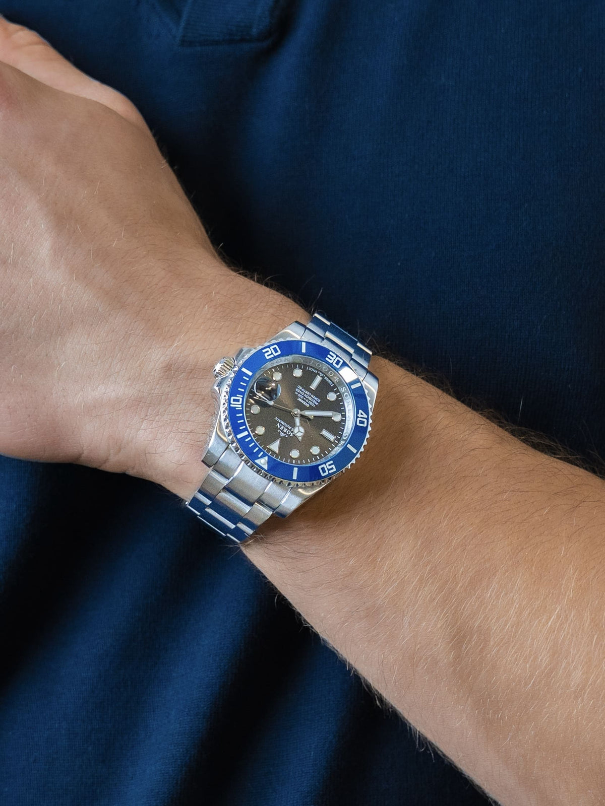 Man wearing the SOREN Oceanic Swiss automatic dive watch, blue bezel on a 3-link steel bracelet, with hand resting on his chest