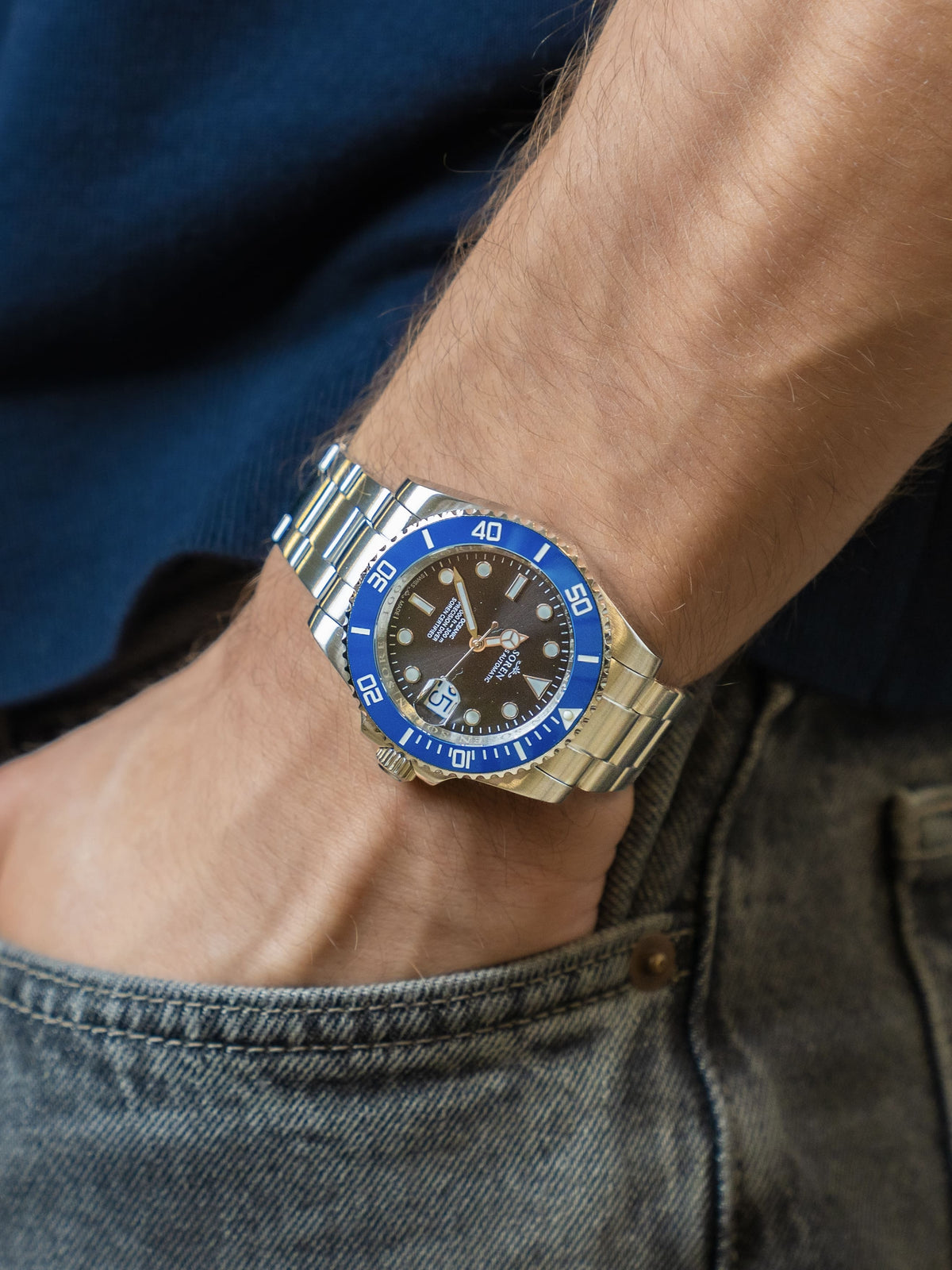 SOREN Oceanic Swiss automatic dive watch with a blue bezel on a 3-link steel bracelet, worn on the wrist with hand in pocket
