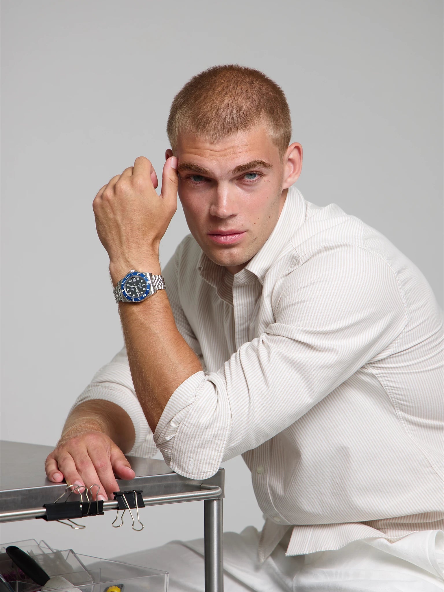 Man wearing a SOREN oceanic blue watch on a jubilee bracelet, seated with his arm on a table
