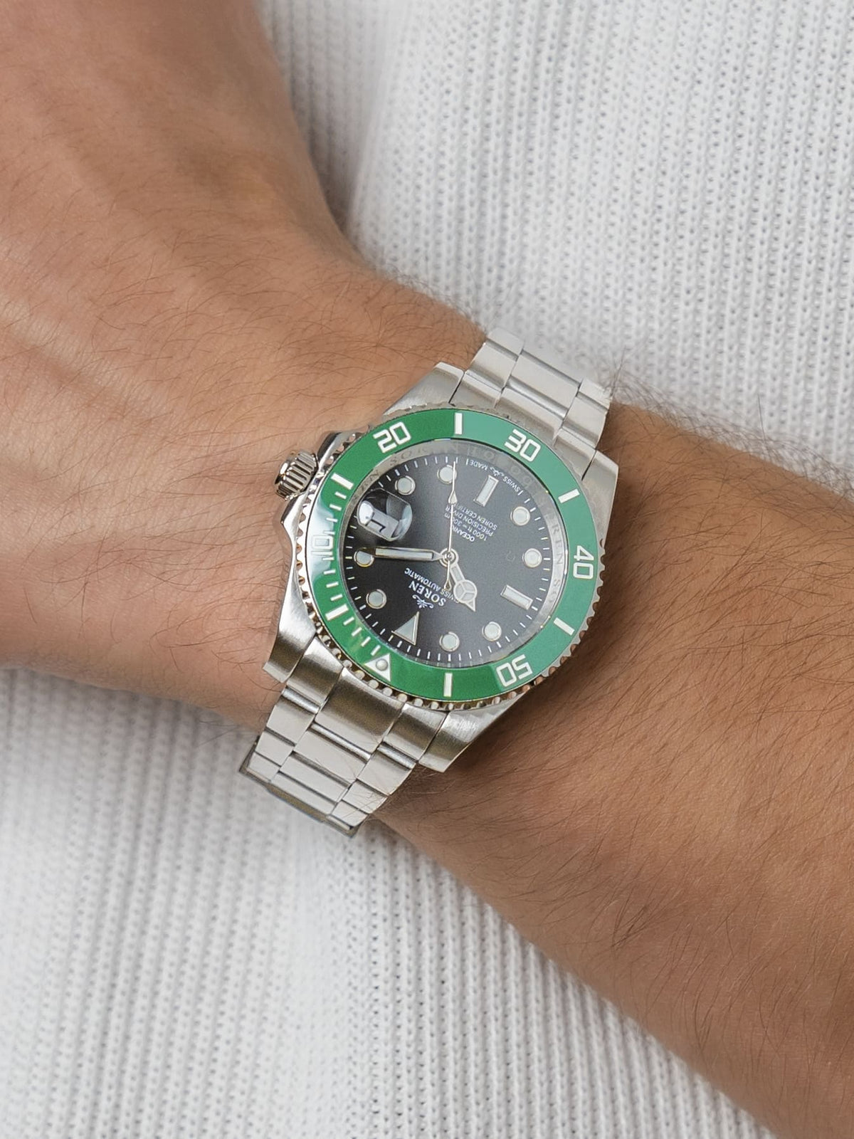 Man wearing the SOREN Oceanic Swiss automatic dive watch, green bezel on a 3-link steel bracelet, with hand resting on his chest