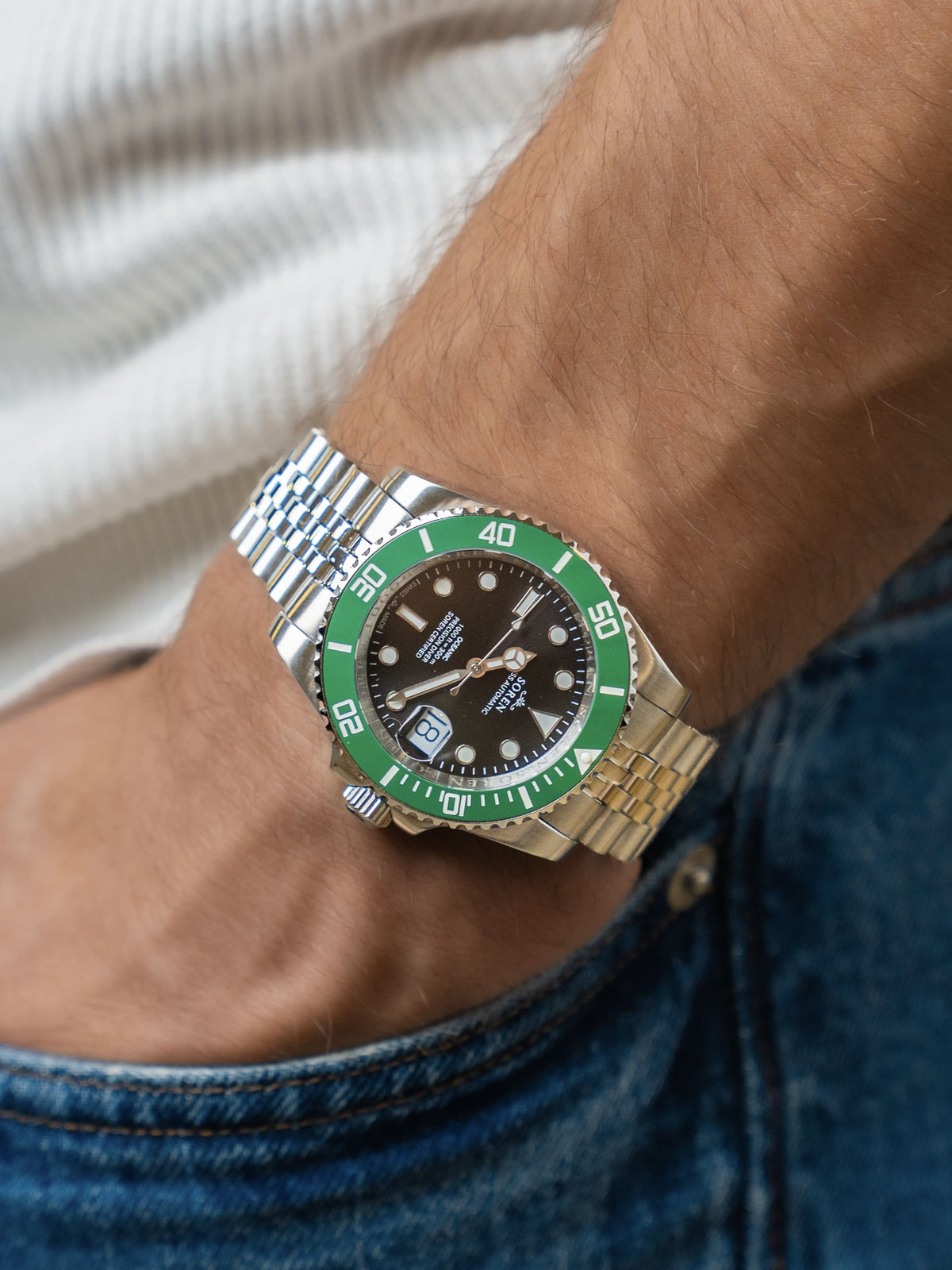 SOREN Oceanic Swiss automatic dive watch with a green bezel and a black dial on a 5-link steel bracelet, worn on the wrist with hand in pocket
